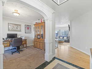 Office space featuring inlaid floor details, decorative columns, a textured ceiling, light carpet, and ornamental molding
