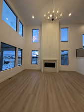 Unfurnished living room with wood finished floors, a chandelier, a high ceiling, a fireplace, and recessed lighting