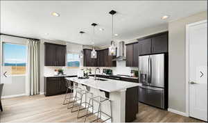 Kitchen with stainless steel fridge, a breakfast bar, wall chimney exhaust hood, dark brown cabinets, and a kitchen island with sink