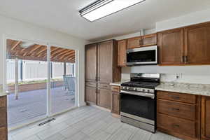 Kitchen featuring appliances with stainless steel finishes, light stone countertops, and brown cabinetry