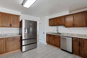 Kitchen with appliances with stainless steel finishes, light stone countertops, and brown cabinets