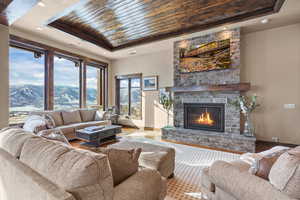 Living area with a raised ceiling, wooden ceiling, a stone fireplace, and wood finished floors