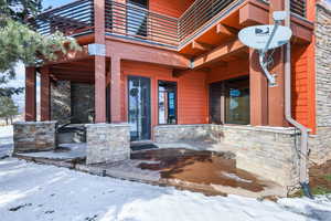 Snow covered property entrance with stone siding and a patio