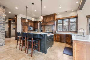 Kitchen with a kitchen bar, decorative light fixtures, light stone counters, a kitchen island with sink, and recessed lighting