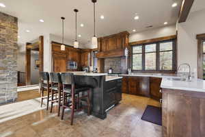 Kitchen with a breakfast bar area, light stone countertops, pendant lighting, backsplash, and a kitchen island