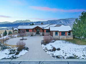 View of front of home featuring a mountain view, a chimney, curved driveway, and stone siding