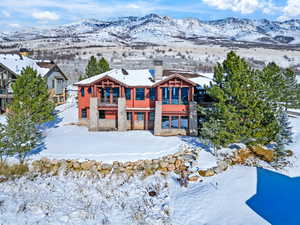 Snow covered property featuring stone siding, a balcony, a chimney, and a mountain view
