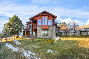 Snow covered property with stone siding, a yard, and a balcony