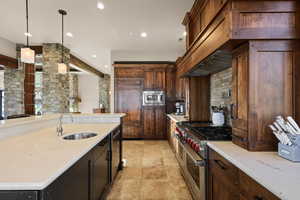Kitchen featuring decorative light fixtures, built in appliances, light stone counters, recessed lighting, and tasteful backsplash