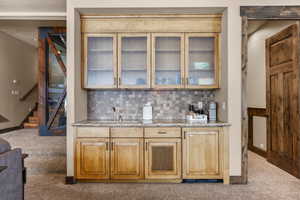 Indoor wet bar featuring light colored carpet, stairway, light stone countertops, and glass insert cabinets