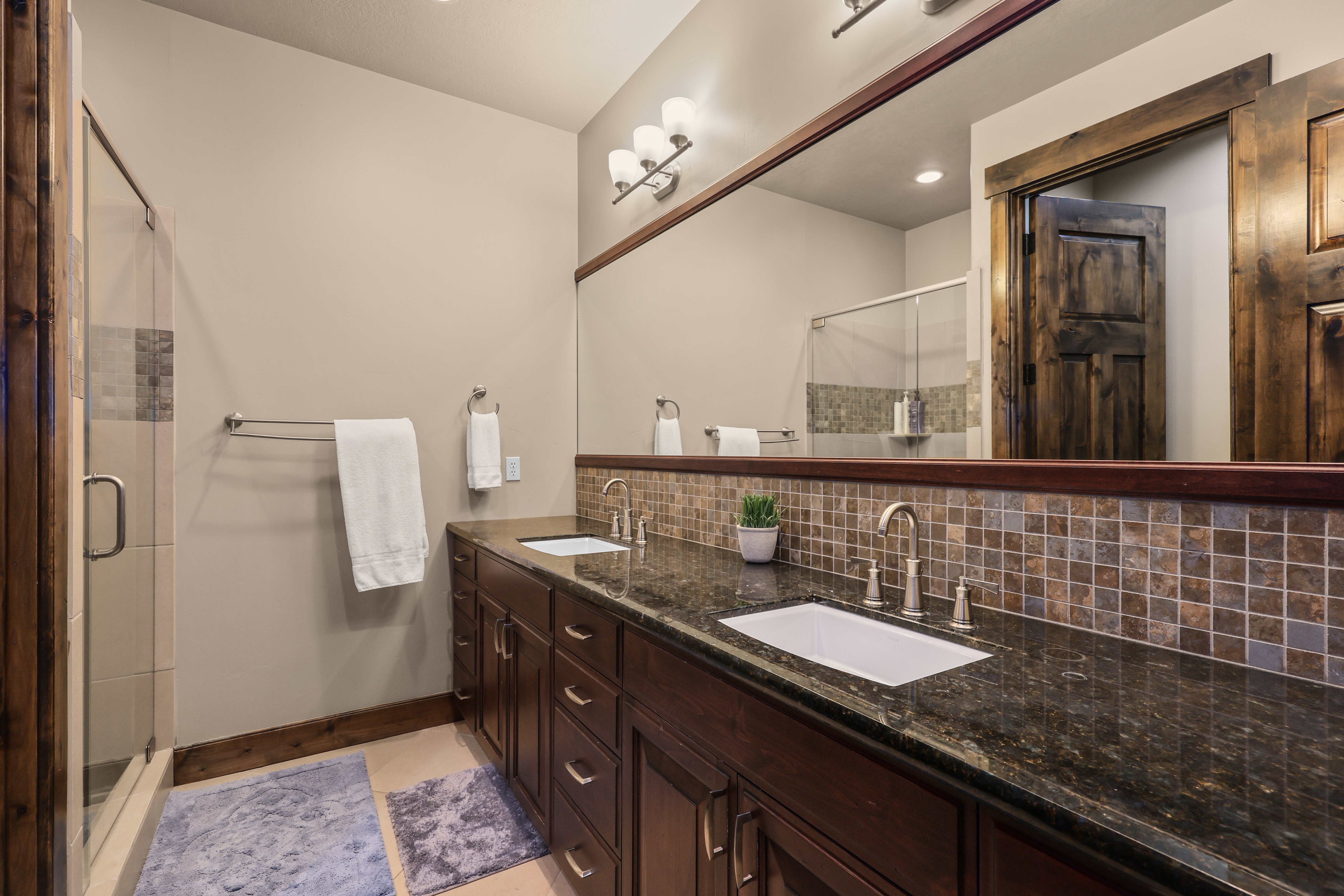 Full bathroom with backsplash, double vanity, and a stall shower