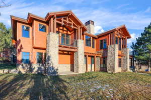 Rear view of property featuring a balcony, a yard, a chimney, and stone siding