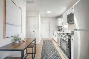 Kitchen with appliances with stainless steel finishes, white cabinets, light countertops, light wood-type flooring, and a textured ceiling