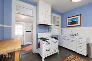 Kitchen featuring white gas stove, white cabinetry, light countertops, custom range hood, and wainscoting