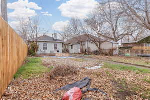 Rear view of house with a fenced backyard, a patio area, a chimney, an outdoor structure, and roof with shingles