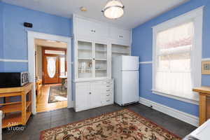 Kitchen with white cabinetry, freestanding refrigerator, stainless steel microwave, glass insert cabinets, and dark tile patterned floors