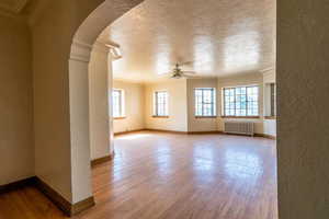 Spare room featuring a textured wall, arched walkways, a textured ceiling, radiator heating unit, and healthy amount of natural light