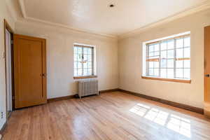 Empty room featuring radiator, a textured ceiling, crown molding, a textured wall, and light wood-type flooring