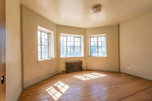 Empty room featuring healthy amount of natural light, light wood-style floors, and radiator