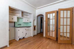 Kitchen featuring white cabinets, arched walkways, decorative backsplash, crown molding, and dark countertops
