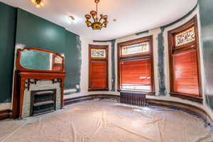 Unfurnished bedroom with radiator heating unit, a chandelier, and a fireplace