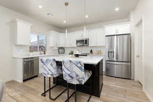 Kitchen featuring stainless steel appliances, white cabinetry, decorative light fixtures, light stone countertops, and decorative backsplash