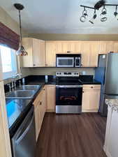 Kitchen with light wood finish cabinets, stainless steel appliances, pendant lighting, and dark wood-style floors