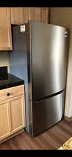 Kitchen view of dark countertops, light wood finish cabinetry, freestanding refrigerator, and dark wood-type flooring