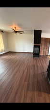 Unfurnished living room featuring dark wood-style floors, a large fireplace, and a ceiling fan