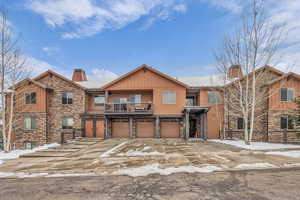 View of front of home featuring a chimney, stone siding, driveway, and a balcony