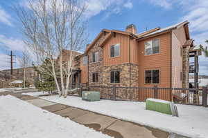View of snow covered exterior with stone siding, board and batten siding, and a chimney