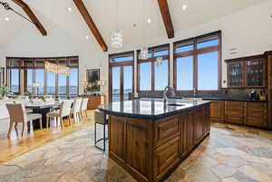 Kitchen with pendant lighting, a kitchen island with sink, high vaulted ceiling, dark stone countertops, and beamed ceiling