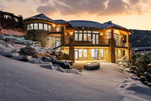 Snow covered rear of property featuring stone siding, a balcony, a patio, and french doors