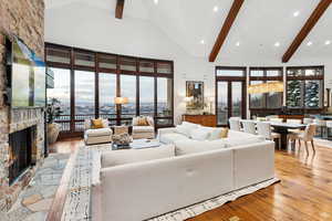 Living area with light wood-style flooring, high vaulted ceiling, a stone fireplace, recessed lighting, and beamed ceiling