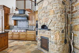 Kitchen with stone tile flooring, brown cabinets, dark stone counters, premium range hood, and a high ceiling