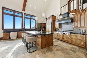 Kitchen featuring decorative light fixtures, a kitchen bar, dark stone countertops, brown cabinets, and high vaulted ceiling