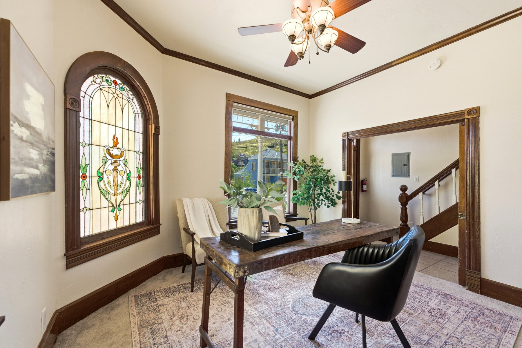 Room featuring a prominent arched stained-glass window, dark wood-finish trim, a ceiling fan with integrated lighting, and a doorway opening to a staircase