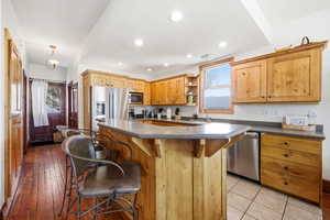 Kitchen featuring a kitchen bar, dark countertops, stainless steel appliances, a center island, and open shelves