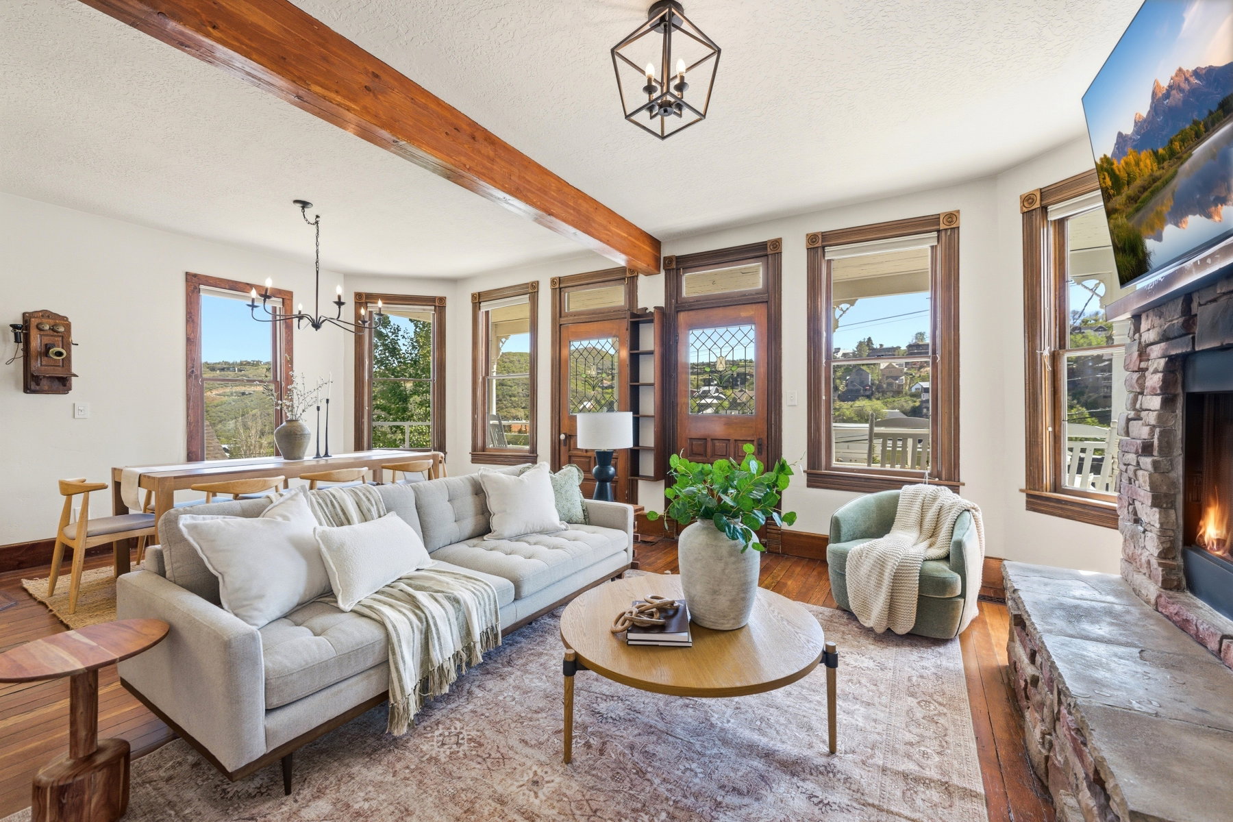 Spacious living area featuring exposed wood beams, a stone-clad fireplace with a hearth, and rich wood-finish flooring