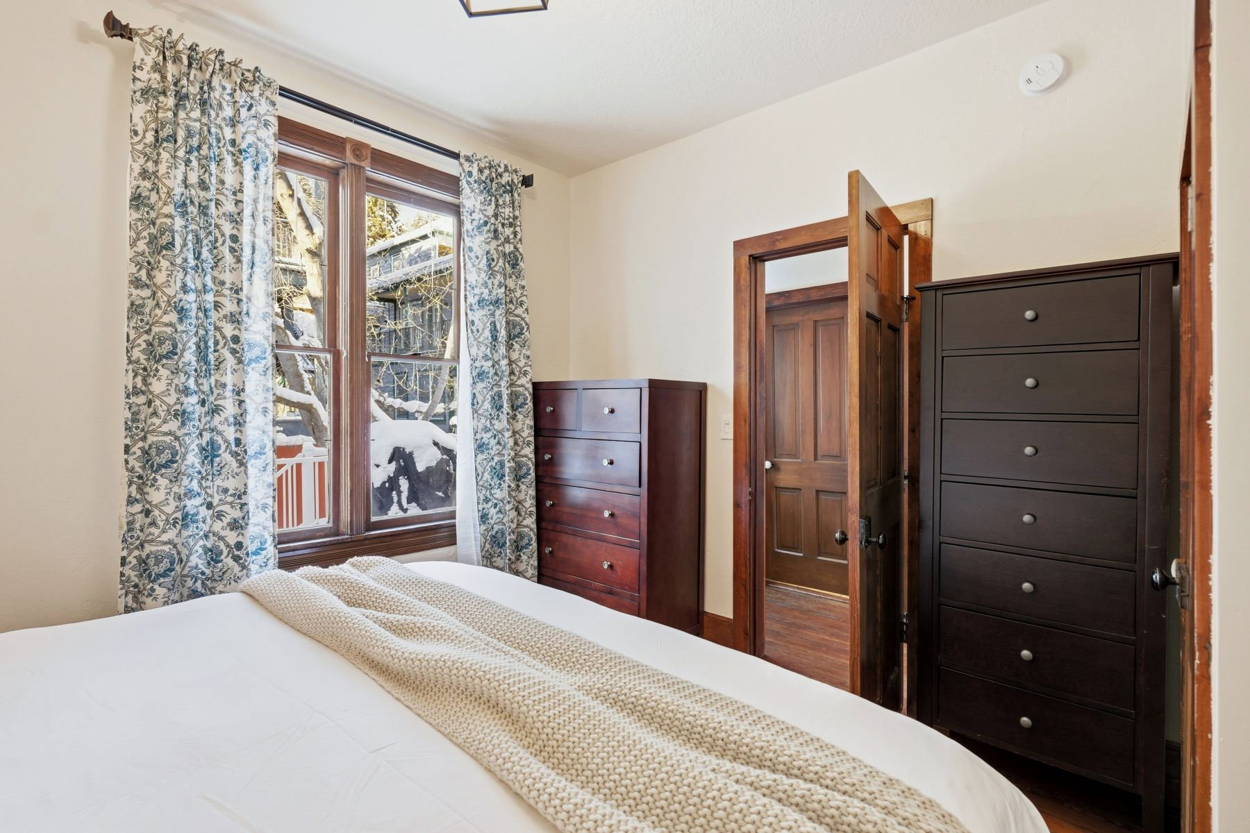 Room featuring a large window with wood trim, patterned curtains, and a wood-panel door