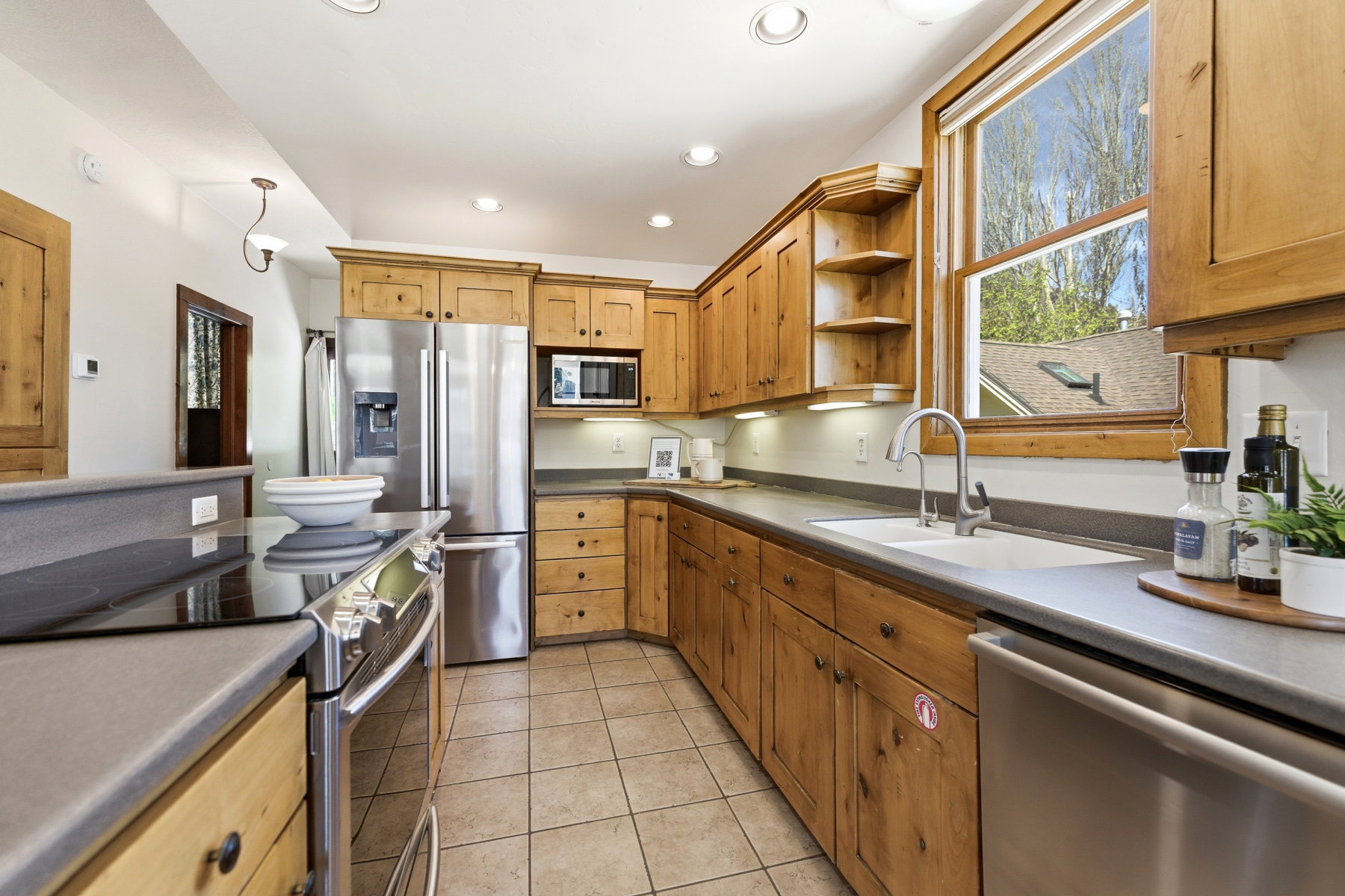 Kitchen featuring wood cabinetry, stainless steel appliances, tiled flooring, solid surface countertops, and an undermount sink
