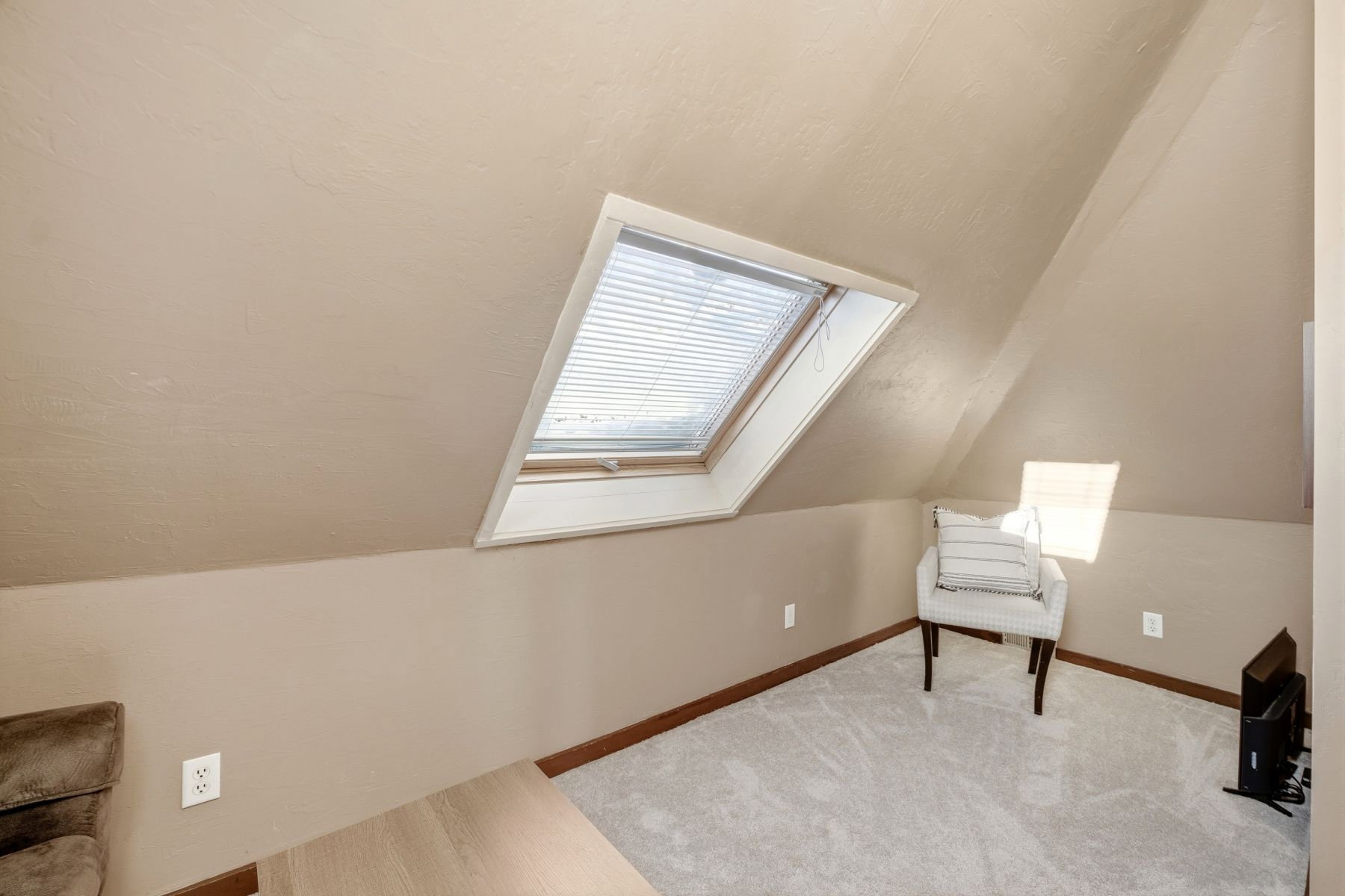 Sloped ceiling room featuring an operable skylight with integrated blinds, light gray carpet flooring, and a baseboard trim