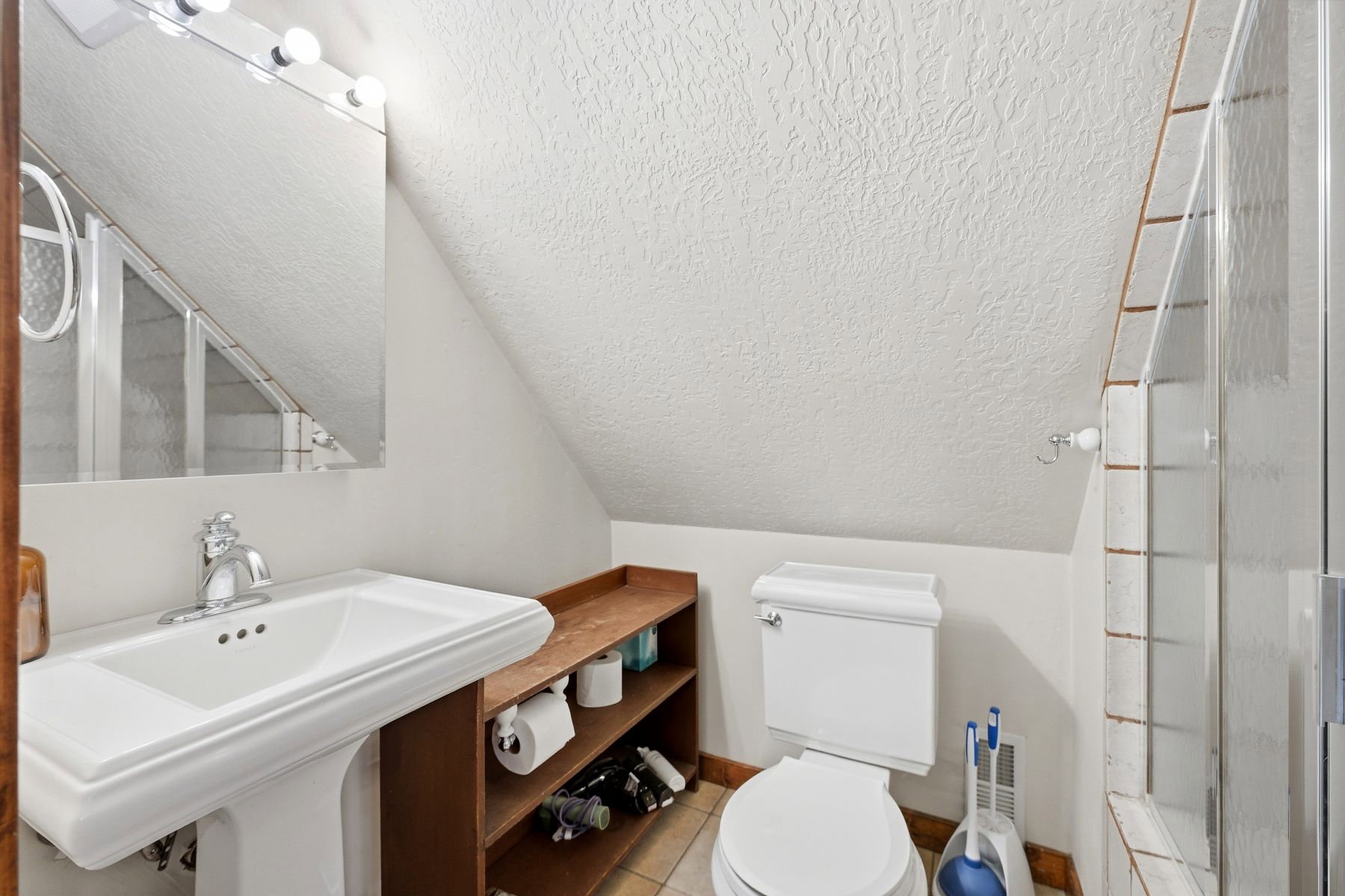 Bathroom featuring a pedestal sink with chrome faucet, a wall-mounted mirror, and an adjacent shower enclosure with clear glass