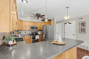 Kitchen featuring dark countertops, backsplash, stainless steel appliances, a ceiling fan, and pendant lighting