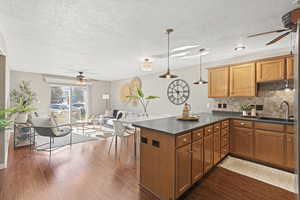 Kitchen featuring ceiling fan, a peninsula, decorative backsplash, hanging light fixtures, and a textured ceiling
