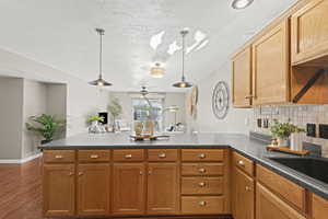 Kitchen with dark countertops, backsplash, a peninsula, pendant lighting, and a textured ceiling