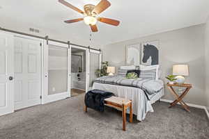 Carpeted primary bedroom with ensuite bathroom, a barn door, plantation shutters and ceiling fan