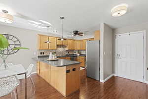 Kitchen with dark countertops, a peninsula, appliances with stainless steel finishes, decorative backsplash, and pendant lighting