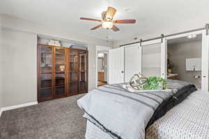 Carpeted primary bedroom with ensuite bathroom, a barn door, plantation shutters, included bookcases and ceiling fan