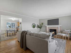 Living area with a tiled fireplace, light wood-style floors, and crown molding